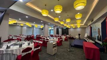 Un salón de conferencias con filas de mesas, sillas y un escenario con un atril.