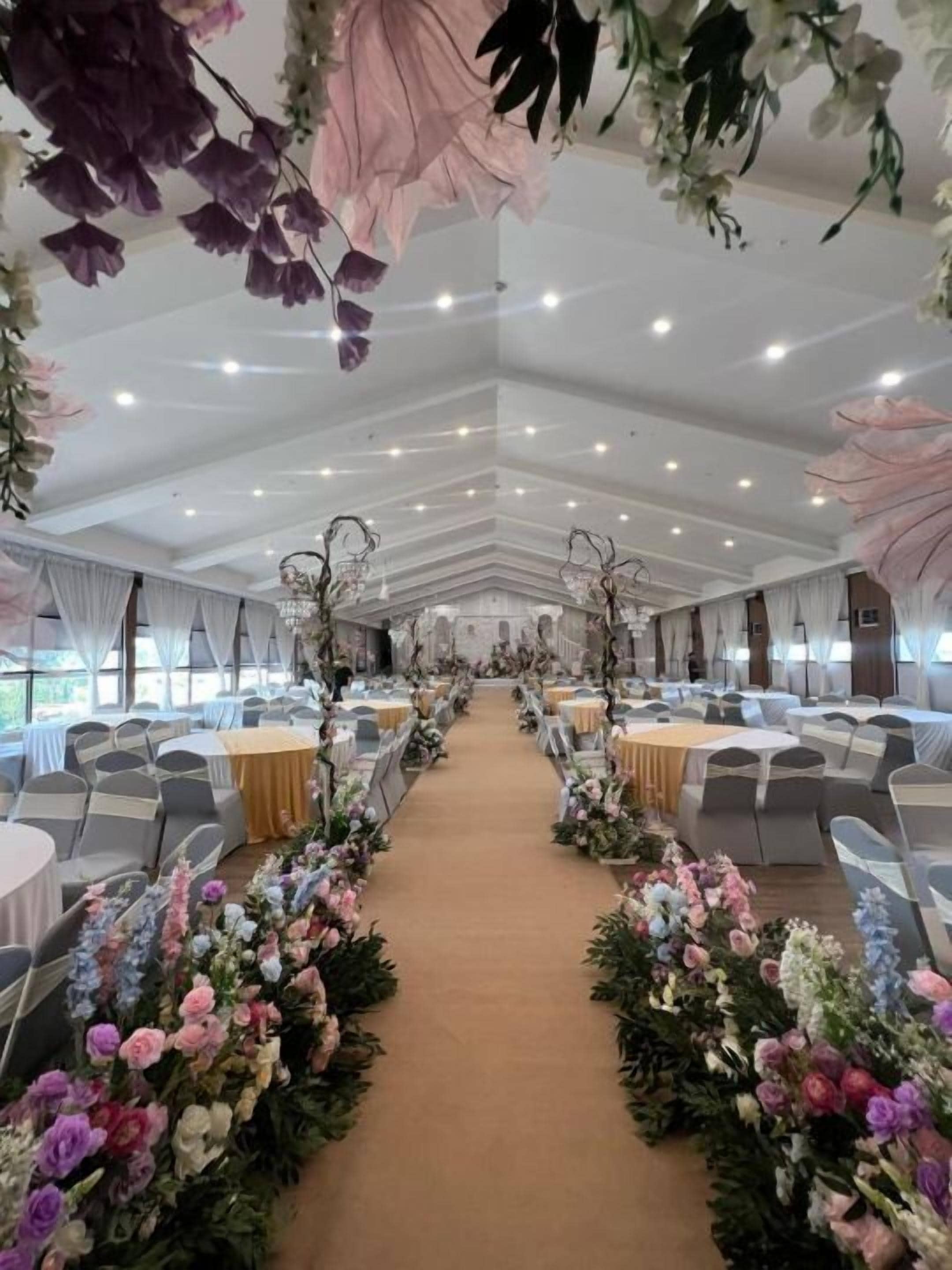 A banquet hall with a central aisle, round tables, and floral decorations.