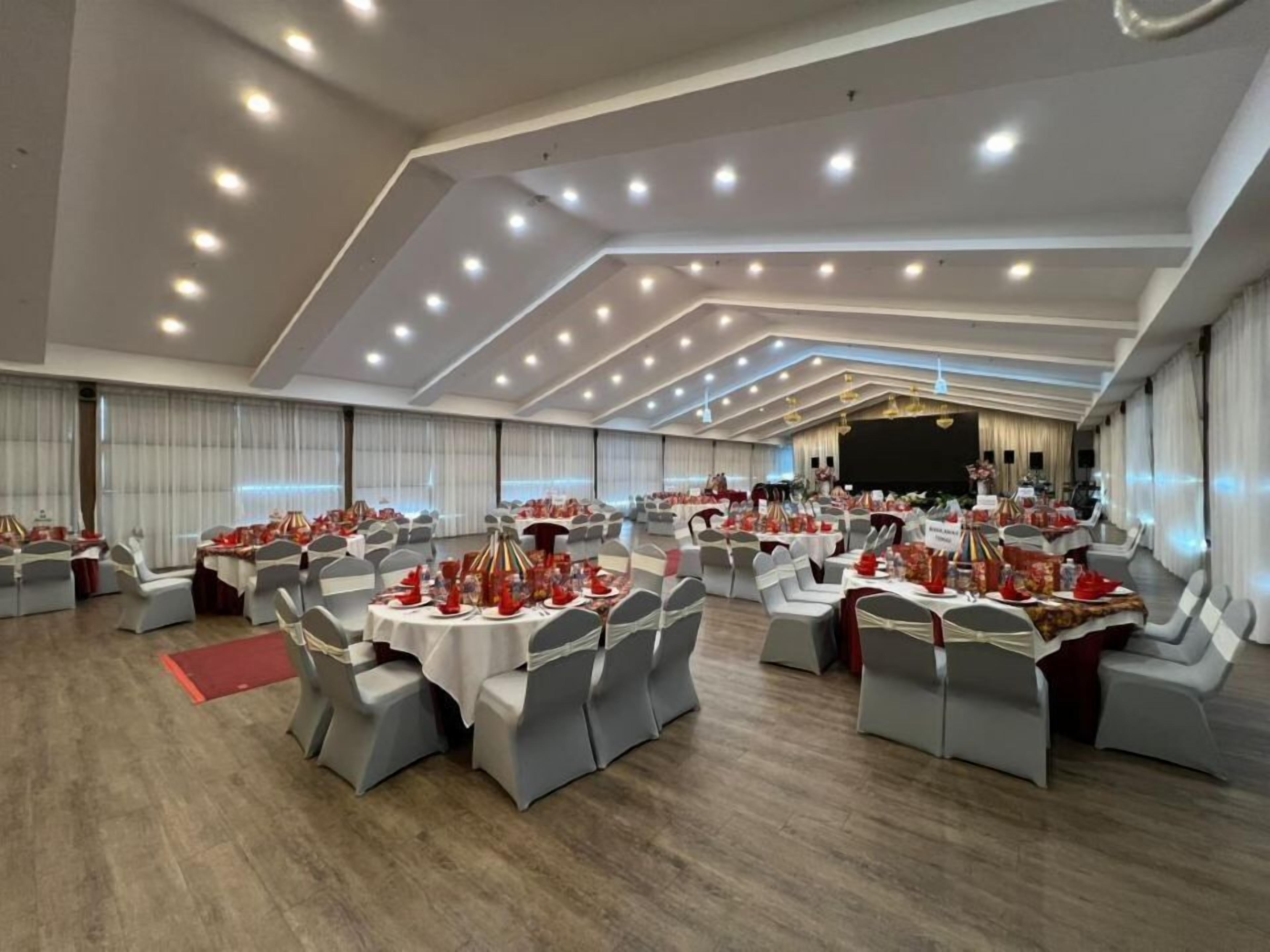 A banquet hall with round tables, grey chairs, and a stage.