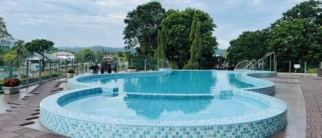 Una piscina con borde de azulejos, rodeada de una terraza de madera y árboles.