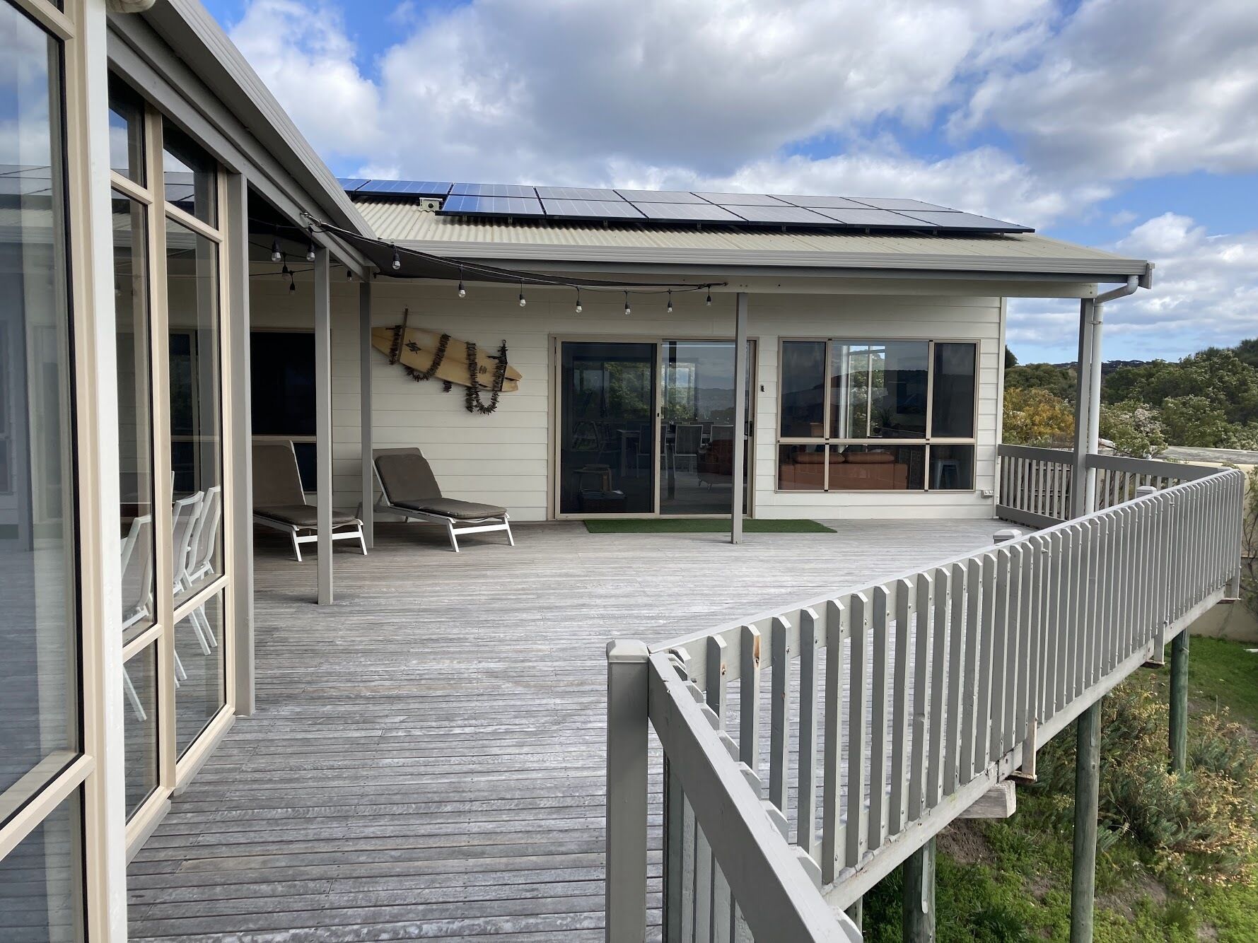 Une maison moderne dotée d’une terrasse en bois, de grandes fenêtres et d’un toit recouvert de panneaux solaires.