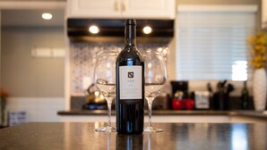 Une bouteille de vin est posée sur un comptoir de cuisine, avec deux verres à vin derrière.