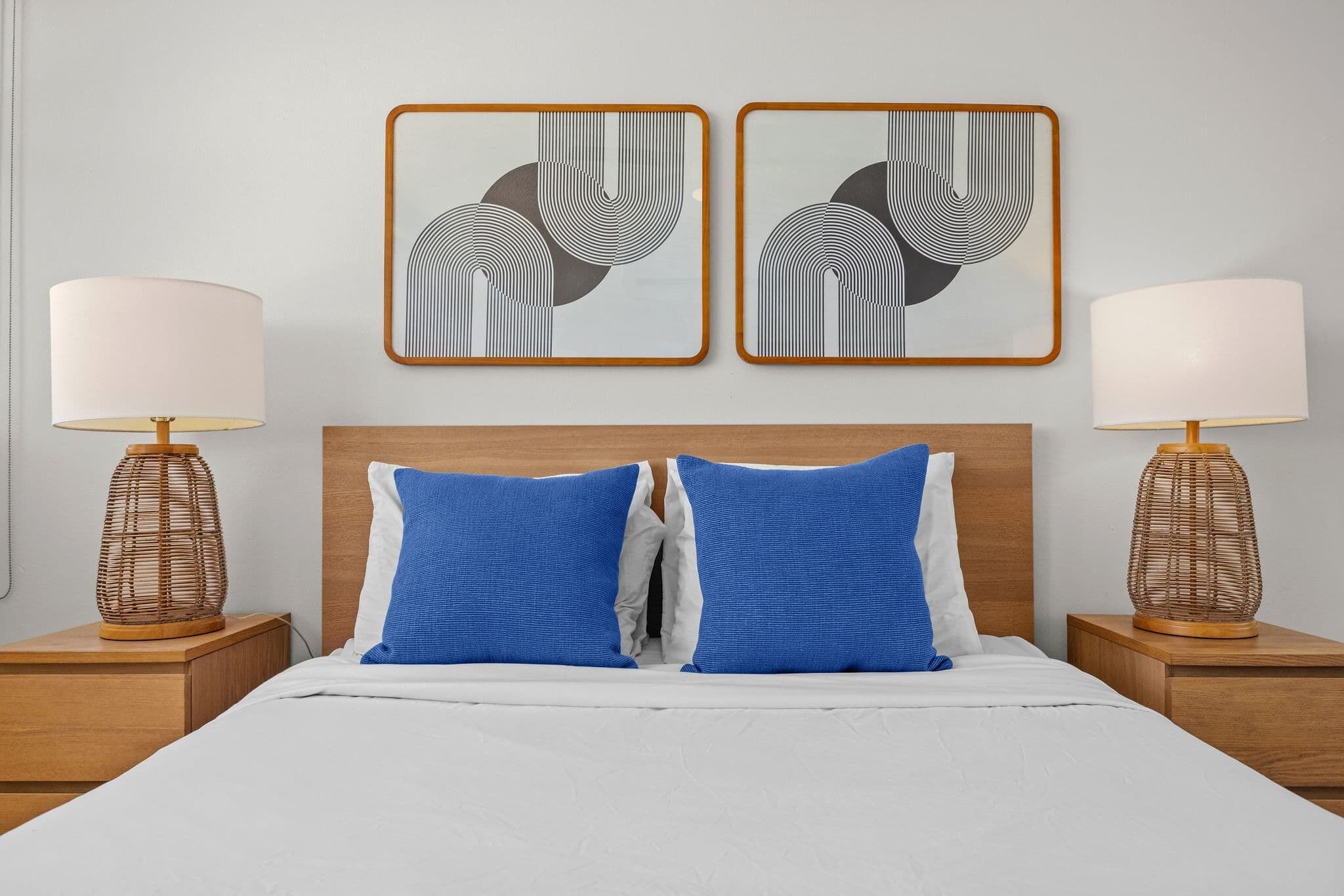A neatly made bed with two blue pillows, a wooden headboard, and two bedside tables with lamps.
