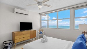 Una camera da letto con un letto, una televisione, una ventola a soffitto, una finestra vista mare e un comò in legno.