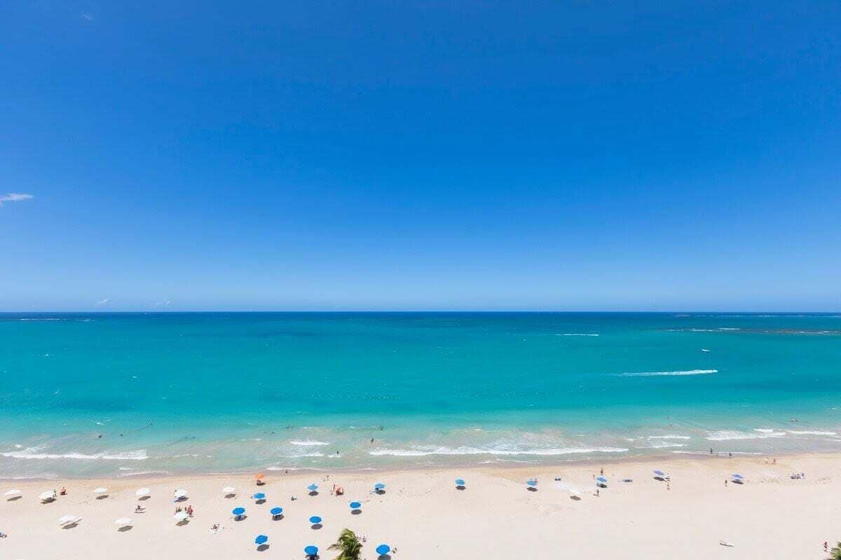 A beach with clear turquoise water, a sandy shore, and several umbrellas.