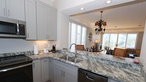 A modern kitchen with grey cabinets, a stainless steel microwave, a built-in oven, a dishwasher, and a marble countertop. - Pet-Friendly 2BR Condo–Cedars East #810 by RVA (Longboat Key)