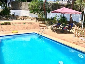 Une piscine avec un bord carrelé, un flotteur jaune et un parasol rose.