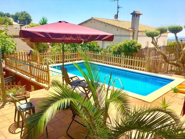 Une piscine avec une terrasse en bois, des chaises longues et un parasol rouge.
