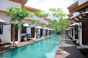 Zona de piscina con cubierta de madera, sillas de descanso y pequeños árboles.