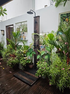 Une terrasse en bois avec un espace douche entouré de différents pots de plantes.