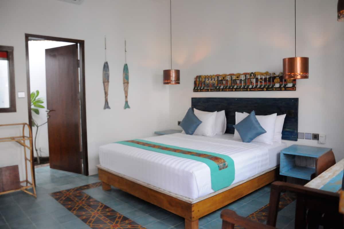 A bedroom with a wooden bed, white bedding, blue pillows, a patterned rug, a wooden nightstand, and a wall art piece.