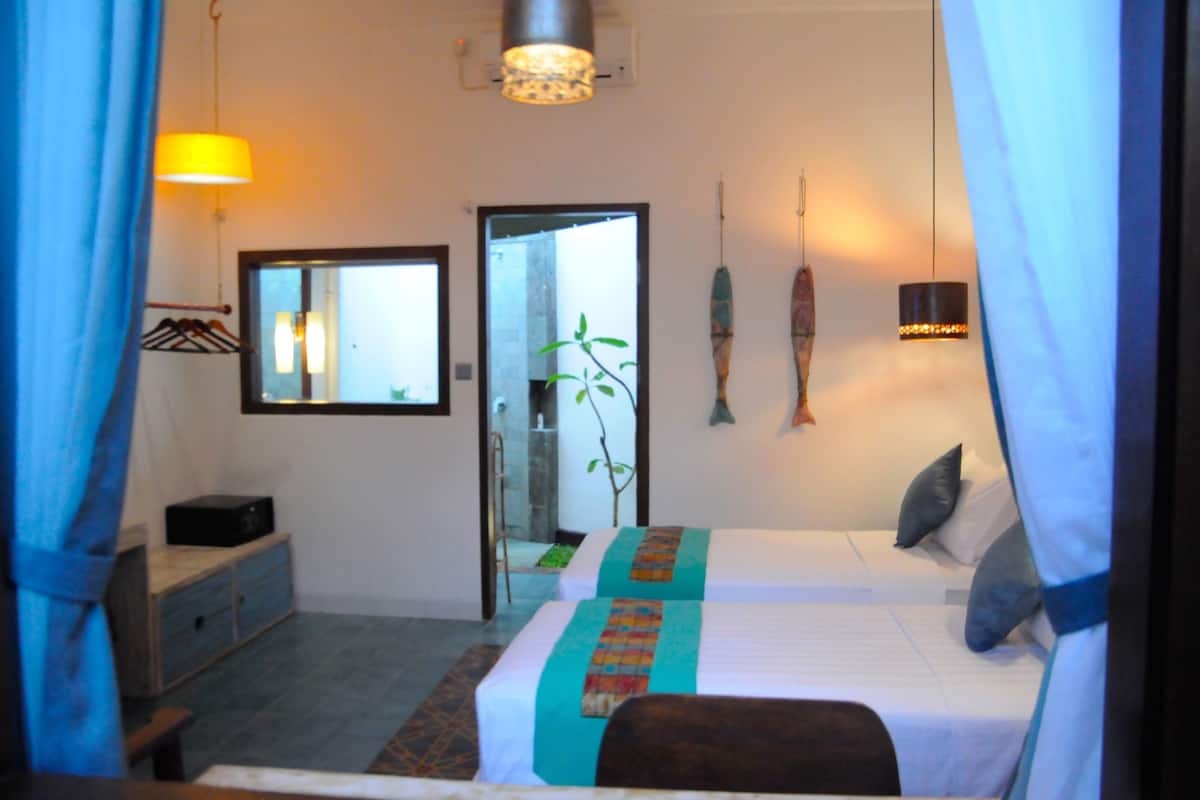 A bedroom with two beds, a bedside table, a mirror, a hanging plant, and a wall-mounted light fixture.