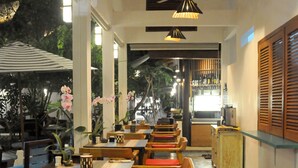 Un restaurante con mesas de madera y sillas con cojines rojos, suelo estampado e iluminación colgante.
