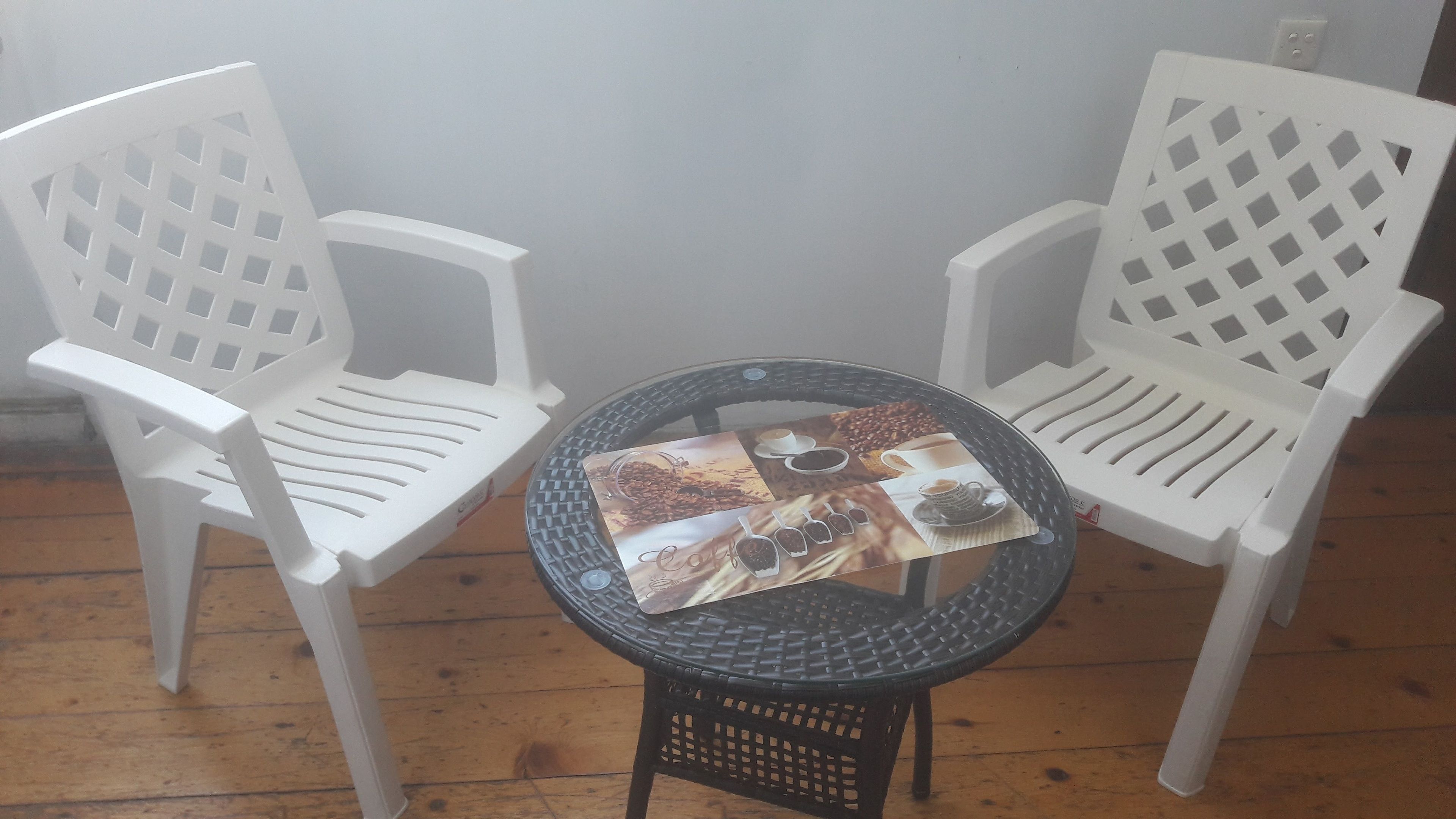 Deux chaises en plastique blanc et une petite table ronde avec un set de table à motifs de café.
