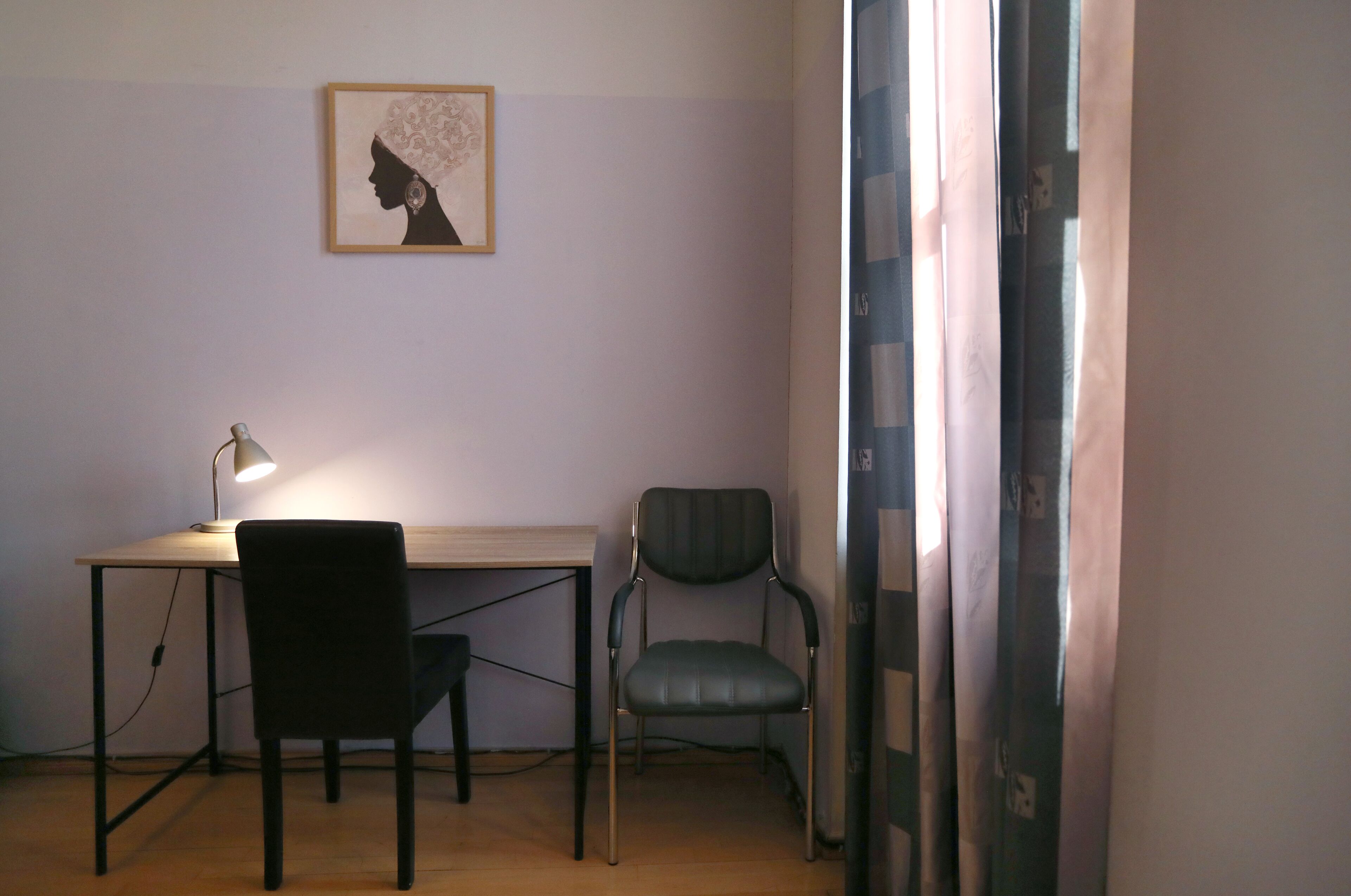A room with a desk, two chairs, a lamp, and a framed artwork on the wall.