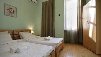 A hotel room with two beds, a wardrobe, a painting on the wall, and a window with curtains.