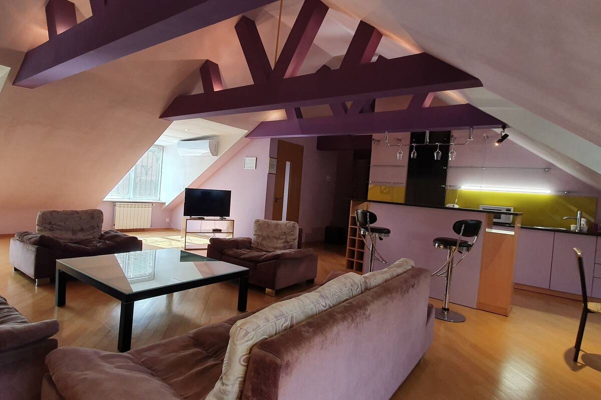 A loft-style living area with a high ceiling, a glass coffee table, and a kitchen with bar stools.