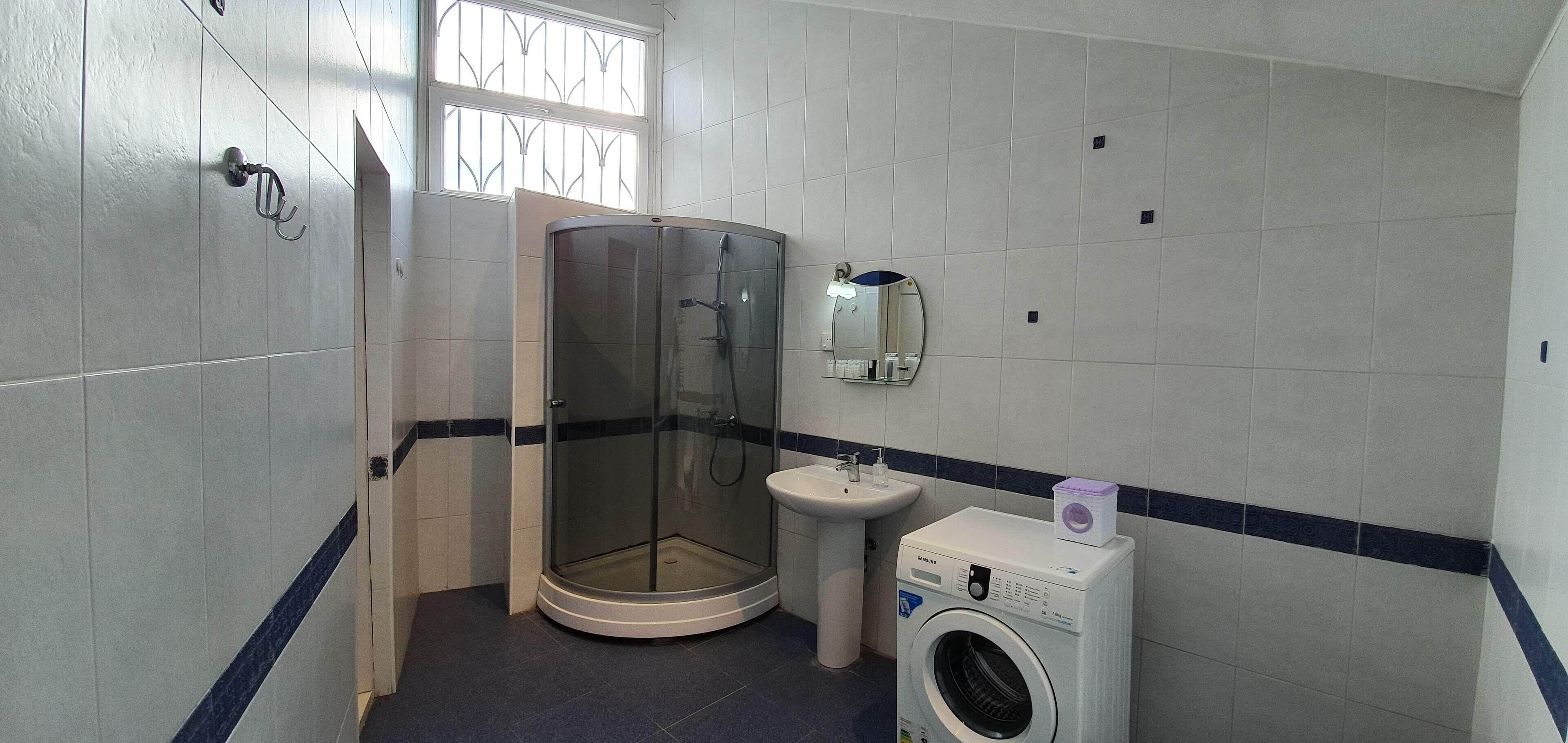 A bathroom with a glass shower enclosure, a sink, and a washing machine.