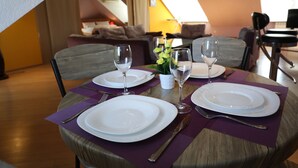 Una mesa de comedor puesta con platos blancos, cubiertos y copas de vino, con individuales morados.