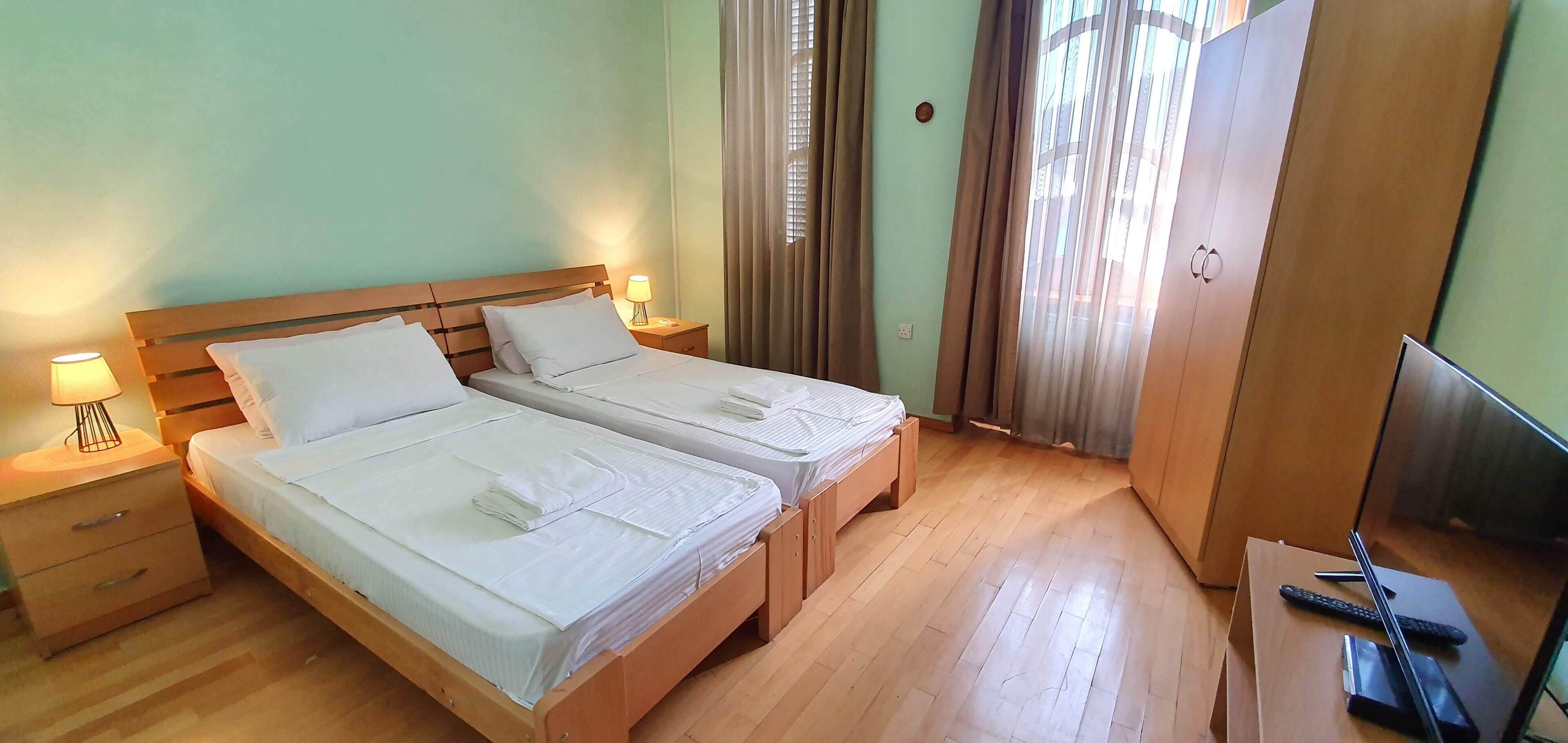 Una habitación de hotel con dos camas, piso de madera, un escritorio con televisor y un armario.
