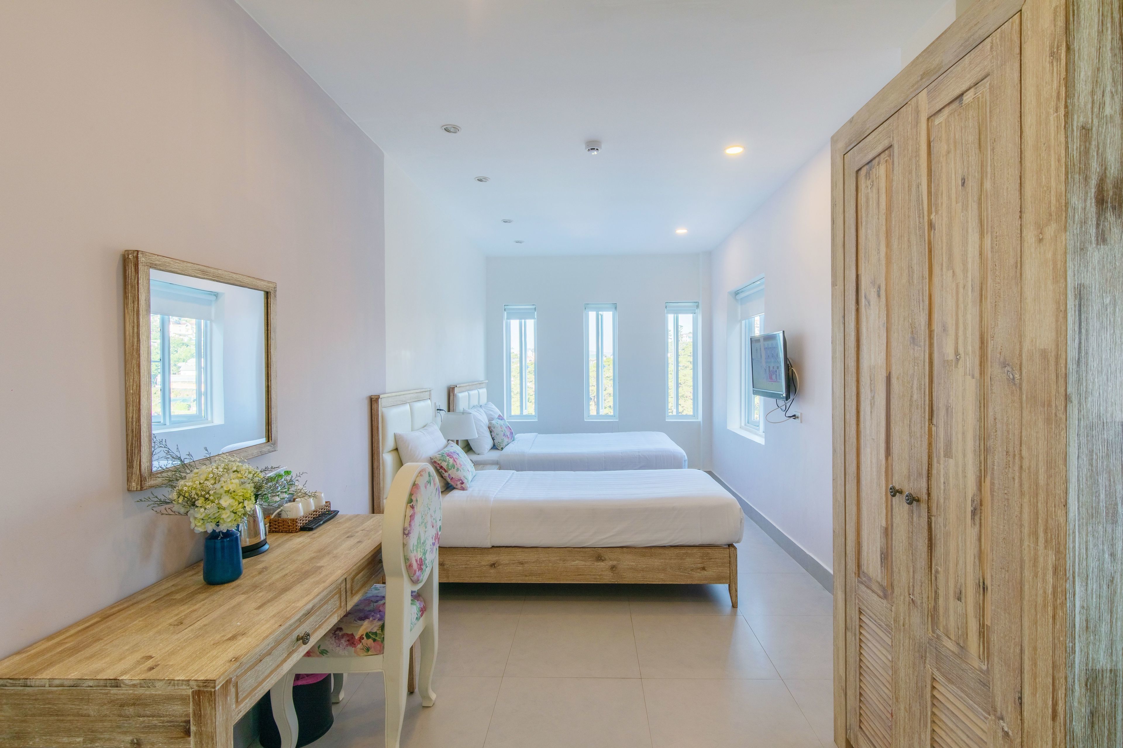 Quarto com cama de madeira, mesa de cabeceira com um vaso de flores e um guarda-roupa grande.