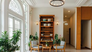 Um quarto espaçoso com uma grande estante de madeira, duas poltronas, uma mesa de centro redonda e plantas em vasos.
