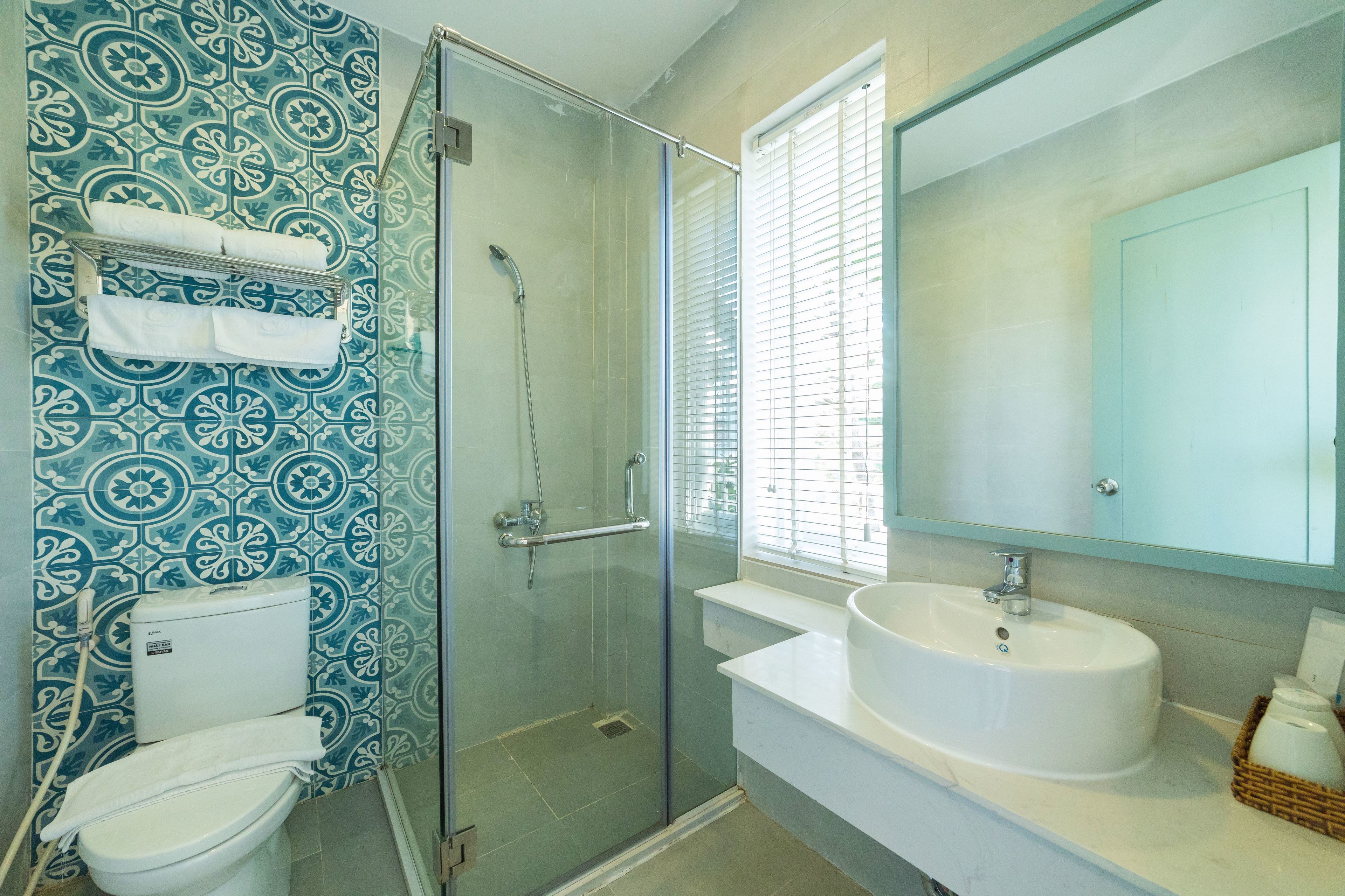 A bathroom with a glass shower enclosure, a white toilet, a sink with a large mirror, and patterned wall tiles.
