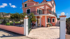 Una casa de dos pisos con un balcón, un camino de entrada pavimentado y un portón.