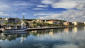 Vista de la costa con un barco amarrado cerca de edificios, palmeras y cielo despejado.