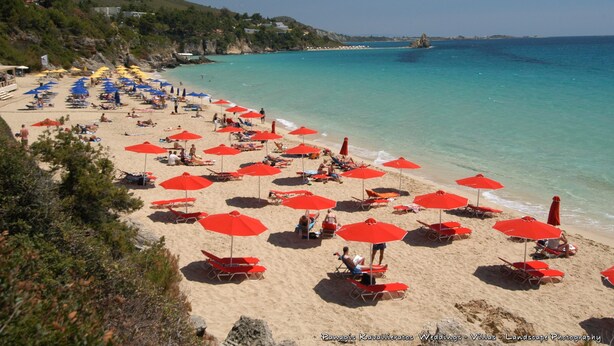 Una playa con numerosas sombrillas rojas y tumbonas.