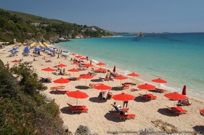 A beach with numerous red umbrellas and sun loungers. - ARTEMIS SUPERB 2 BEDROOM APARTMENT  700 m  AWAY FROM  THE BEACH (CEPHALONIA)