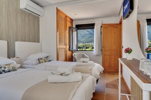 A hotel room with two beds, a wooden wardrobe, a TV, and a view of mountains.