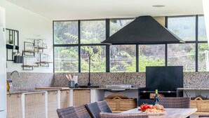 Una cocina moderna con ventanas amplias, una parrilla, mobiliario de mimbre y una mesa de comedor con comida.