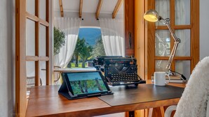 Un escritorio de madera con una computadora portátil, una máquina de escribir, una lámpara y una taza.