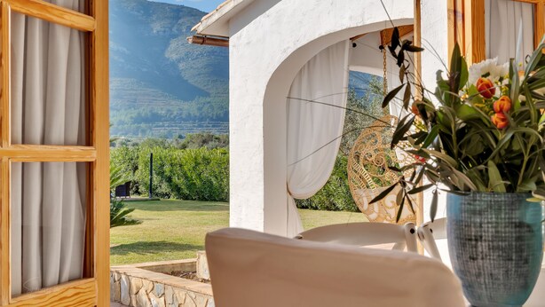 Una habitación con vista a un paisaje montañoso, una pared blanca y una planta colgante.