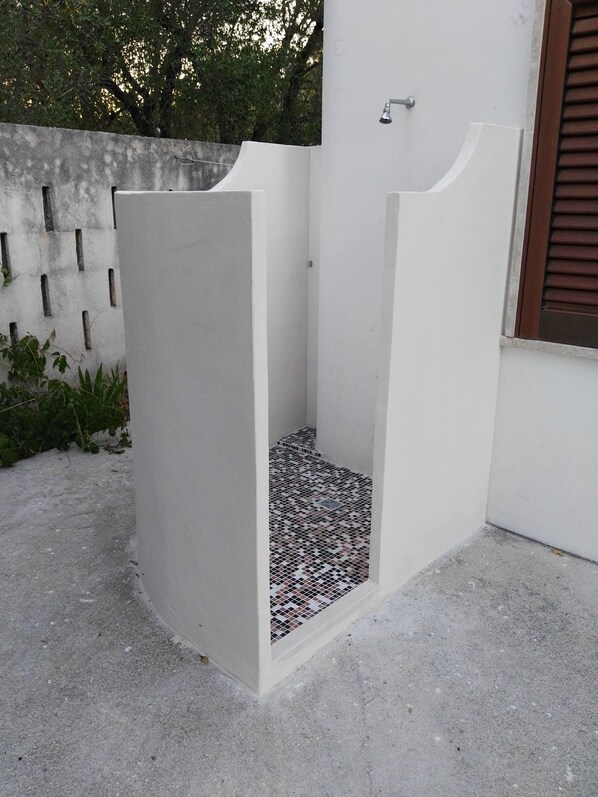 A modern outdoor shower area with a tiled floor and a white wall.
