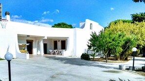 Un edificio moderno blanco con un patio cubierto, mobiliario exterior y un aro de baloncesto.