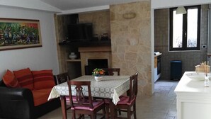 Una sala de estar con un sofá, una mesa de comedor con sillas, una chimenea y una zona de cocina con una ventana.