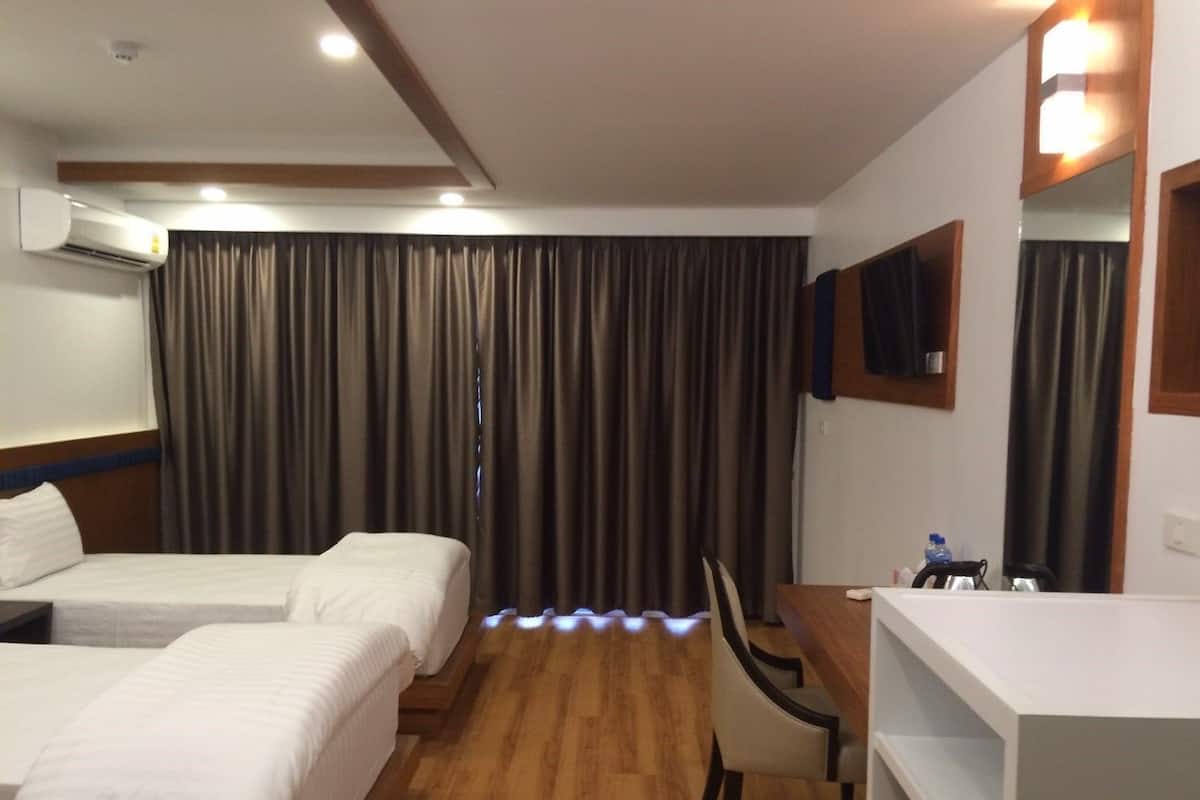 Habitación de hotel con dos camas, un escritorio, una silla, un televisor de pantalla plana y un equipo de aire acondicionado.