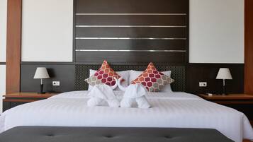 A neatly made bed with white linens, two decorative pillows, and a grey ottoman.