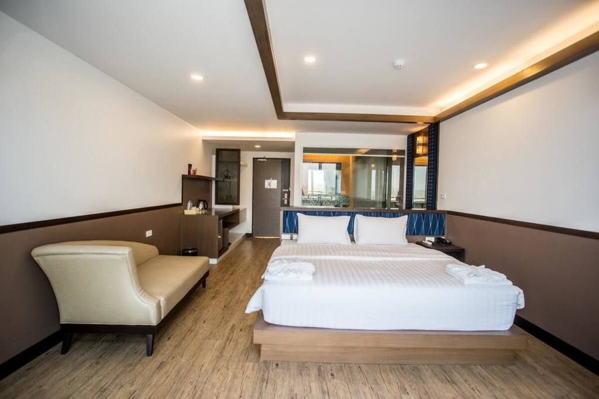 Habitación de hotel con una cama grande, una silla, un escritorio, un espejo y un baño visible a través de una puerta abierta.