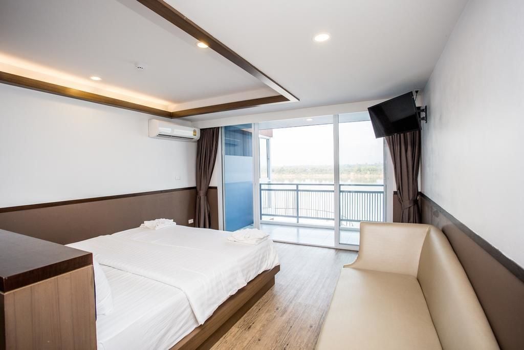 Una habitación de hotel con cama, sofá, televisor montado en la pared y balcón con vistas.