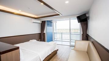 Una habitación de hotel con cama, sofá, televisor montado en la pared y balcón con vistas.