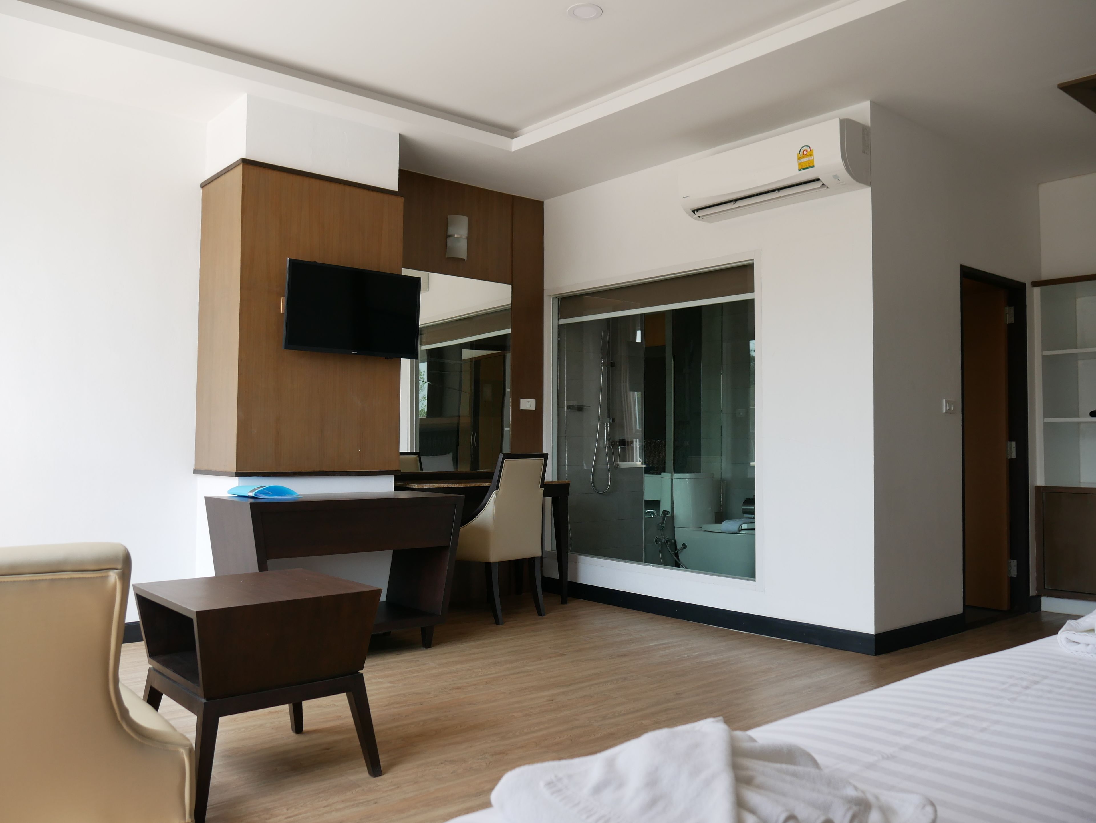 Una habitación de hotel moderna con un escritorio de madera, televisor, armario y zona de ducha.