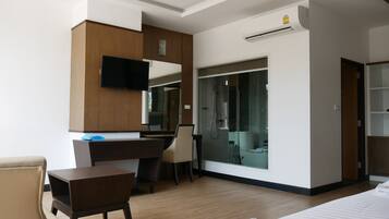 Una habitación de hotel moderna con un escritorio de madera, televisor, armario y zona de ducha.