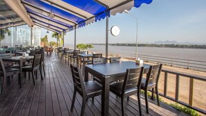 An outdoor dining area with tables and chairs, a covered walkway, and a view of a river.