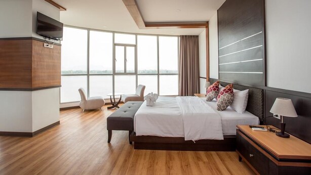 A modern hotel room with a large bed, a TV, a desk, and a view of the city.