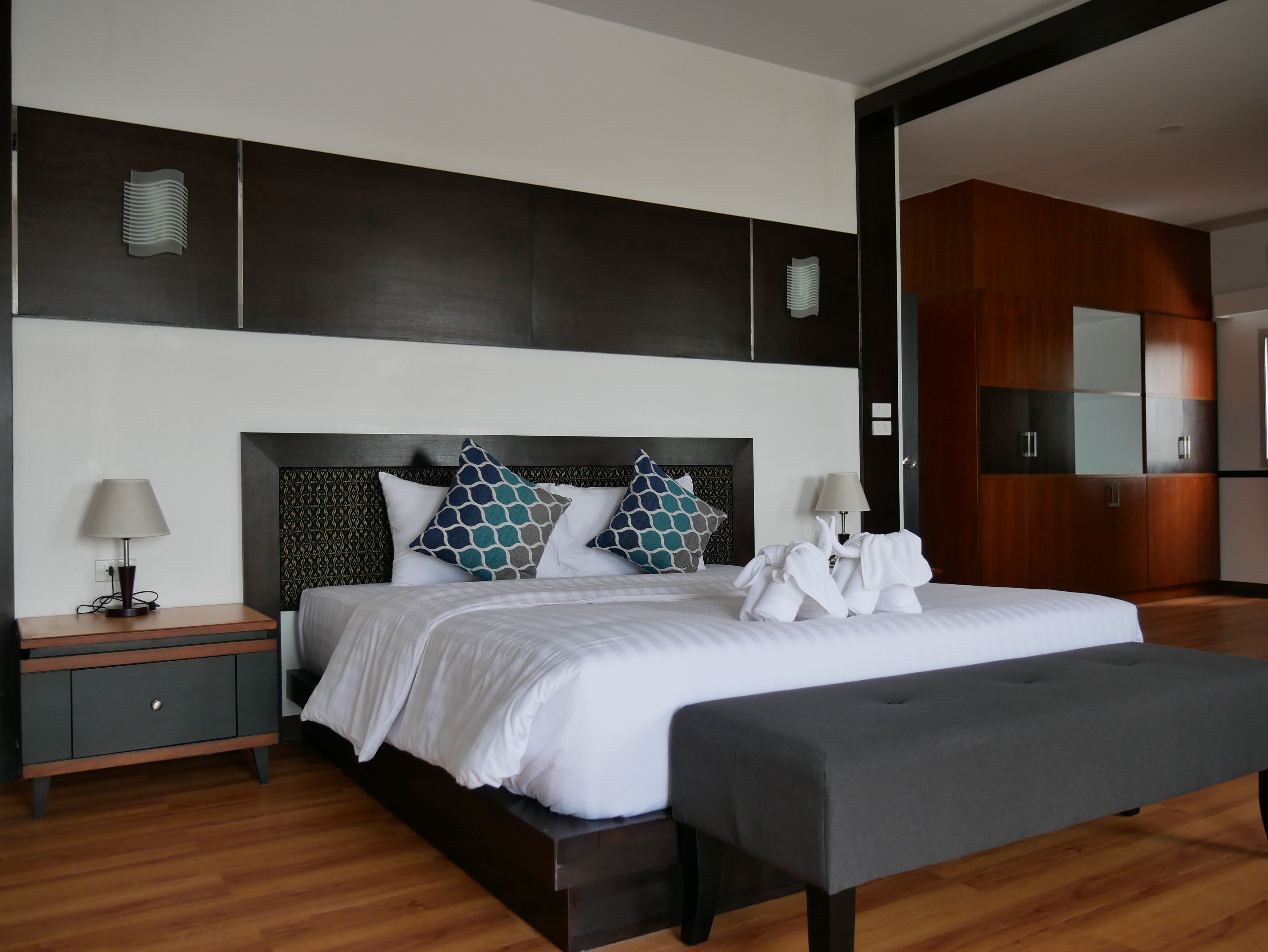 A modern hotel room with a large bed, a bedside table, a bench, and a wardrobe.