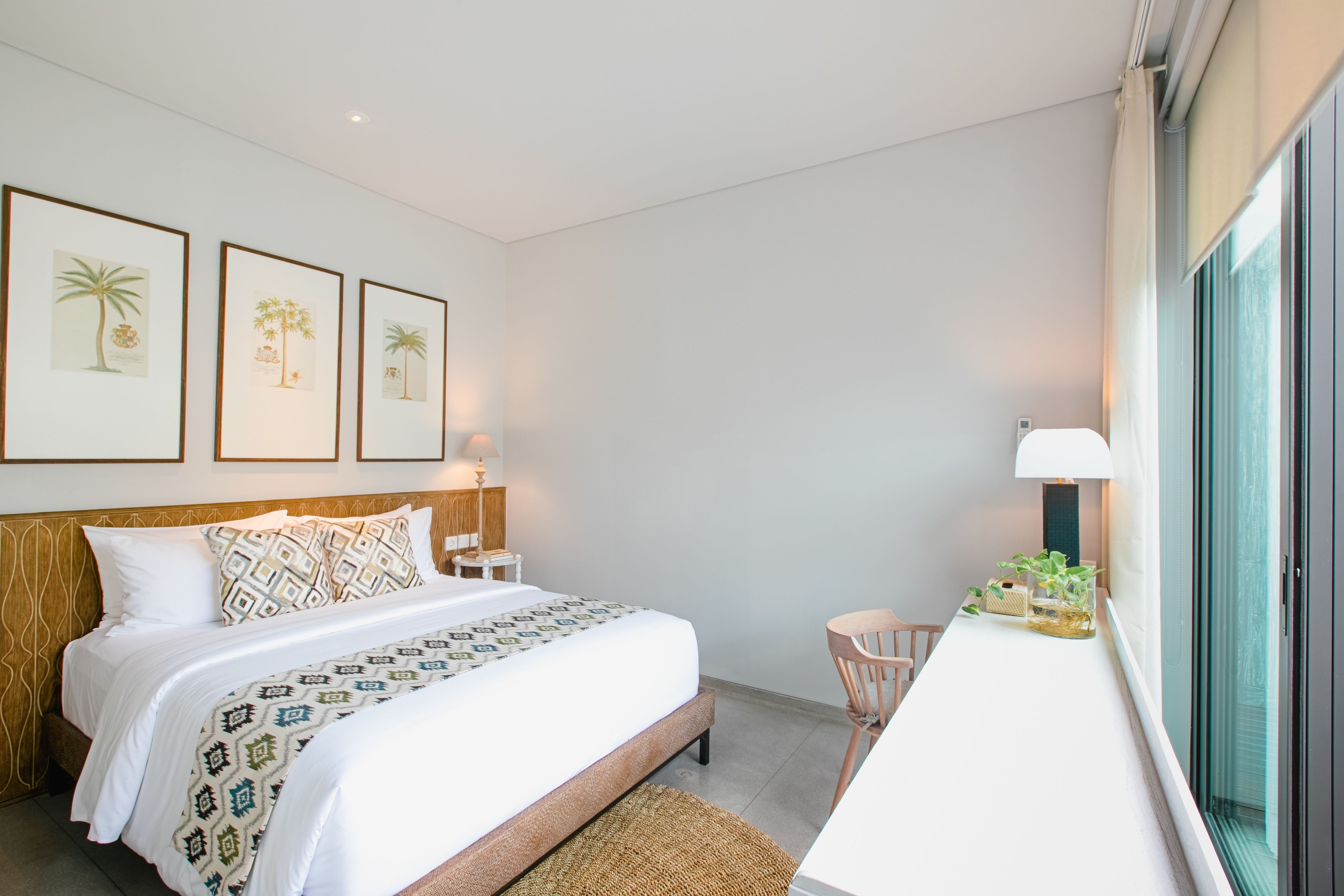 A modern hotel room with a neatly made bed, a small desk with a lamp, and a window with a view.