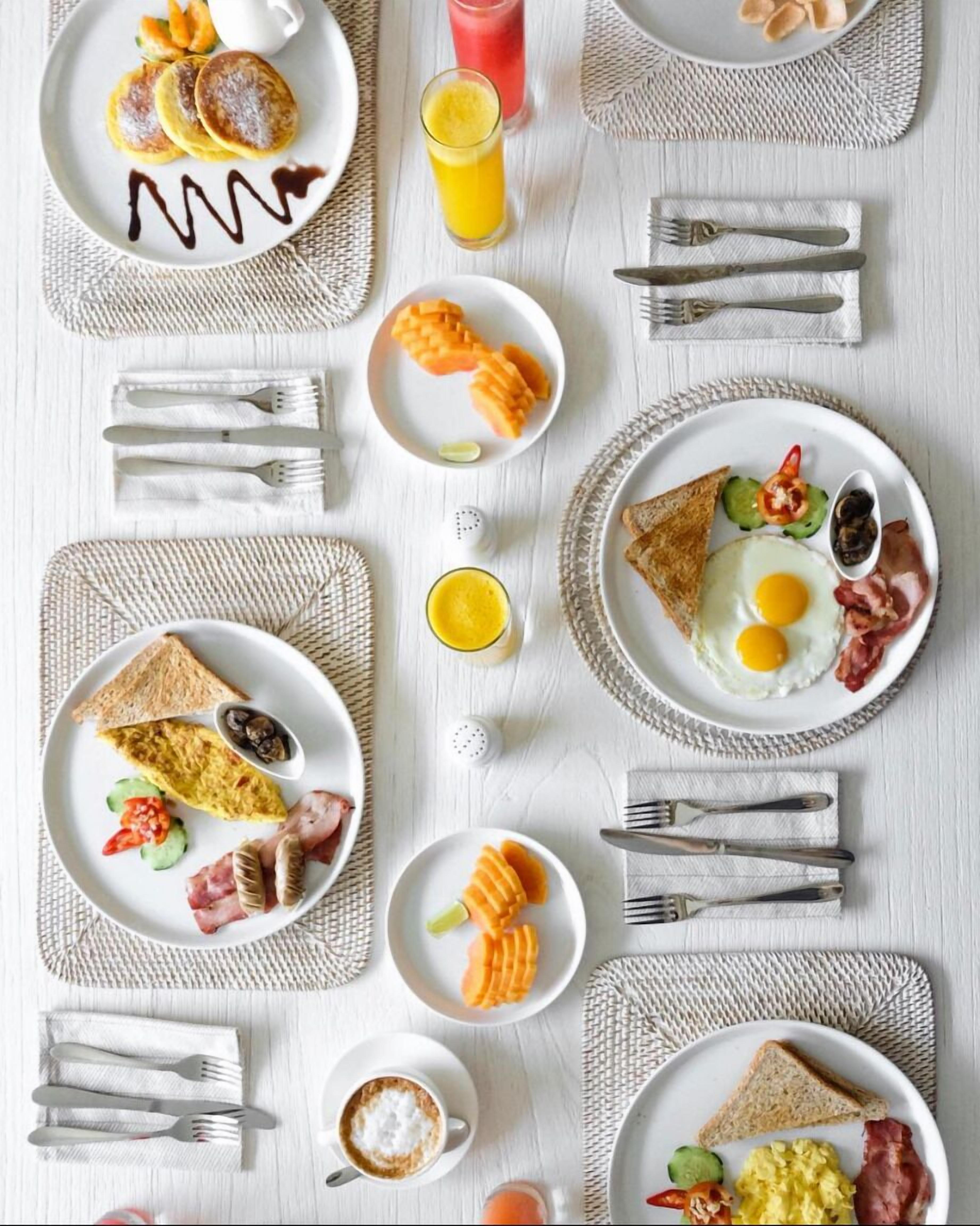 Een ontbijttafel met verschillende borden eten, waaronder eieren, spek, toast en diverse soorten fruit.
